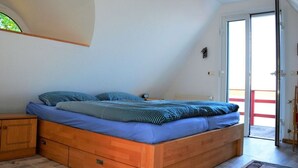 A bedroom with a wooden bed, a nightstand, a window, and a door leading outside. - Holiday House House by the Lake (Krakow am See)