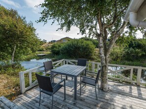 Une terrasse en bois avec une table et des chaises, donnant sur une étendue d’eau et une zone verdoyante.