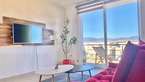 A modern living room with a flat-screen TV, a small table, a red sofa, and a balcony with a view of the mountains. - Alojamiento en Yecapixtla, Morelos. Disfruta con Amigos o Familia! (Yecapixtla)
