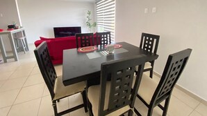 A dining area with a black table and four chairs, a red sofa, and a TV in the background. - Alojamiento en Yecapixtla, Morelos. Disfruta con Amigos o Familia! (Yecapixtla)