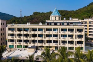 A multi-story building with balconies, a central tower with a blue roof, and a hilly background. - Xiachuan Island Haijiao Hotel (Taishan)