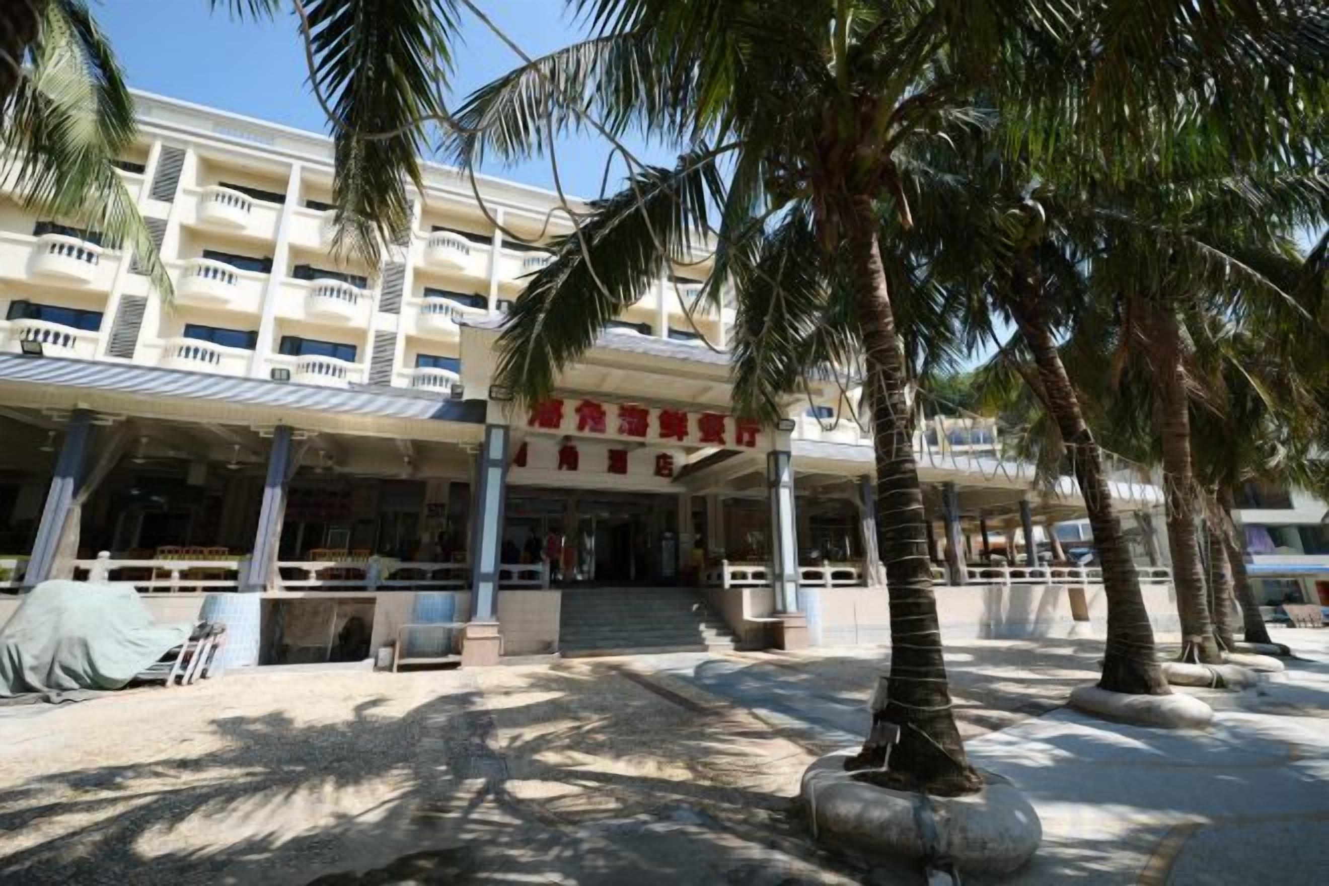A hotel entrance with a covered walkway, palm trees, and a building with multiple floors and balconies.