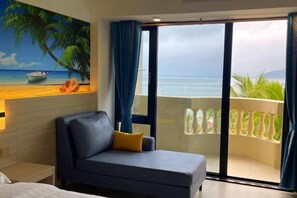 Habitación de hotel con un amplio ventanal corredero que da a un balcón con vistas al océano y palmeras.