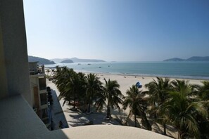 Vista da praia a partir de uma varanda, com palmeiras e céu limpo.