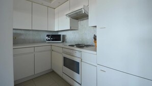 Une cuisine compacte avec des meubles blancs, un four à micro-ondes encastré, une cuisinière et une hotte aspirante.