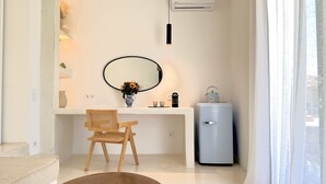 Un baño moderno con un lavamanos blanco, un espejo redondo, una silla de madera, un refrigerador pequeño y un aire acondicionado de pared.