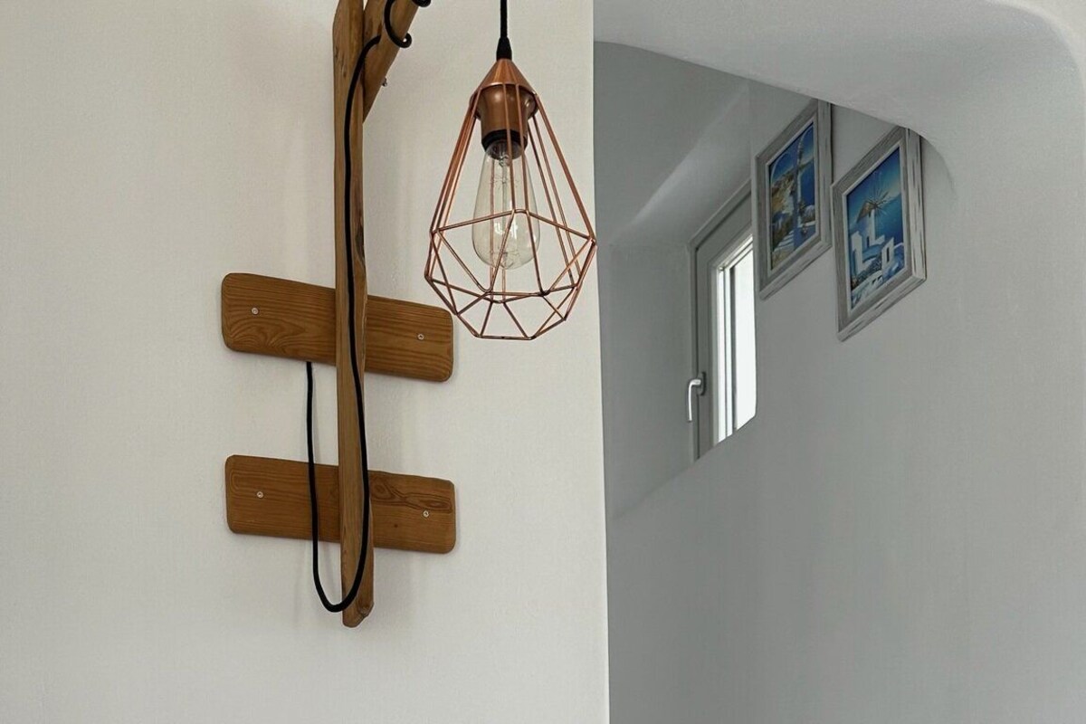 A bedroom with a bed, a bedside table, a wall-mounted light fixture, and a staircase leading to another room.