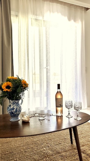 Una mesa con un jarrón de girasoles, una botella de vino, dos copas de vino y una figura decorativa de soldado de hojalata.