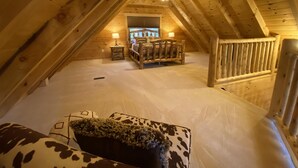 Un dormitorio en el ático con techo inclinado de madera, una cama con cabecera, una mesita de noche y una lámpara.