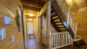 Un intérieur en bois avec un escalier et un couloir menant à une porte.
