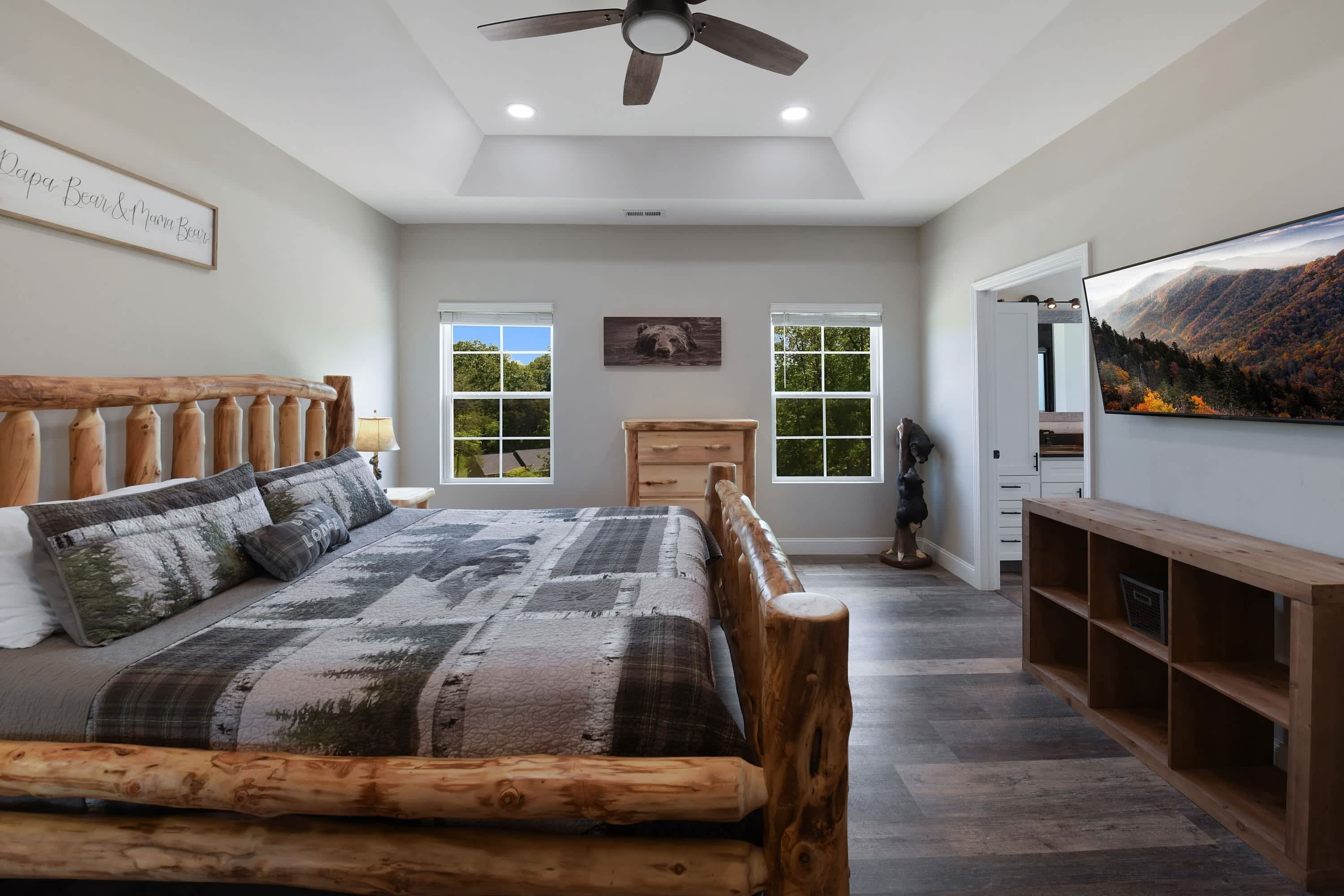 Un dormitorio con cama de madera, ventilador de techo, ventana grande y televisor montado en la pared.