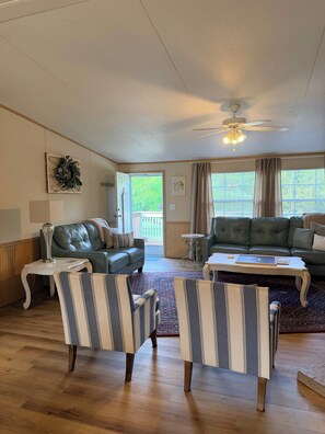 Ein Wohnzimmer mit einem grünen Sofa, gestreiften Ohrensesseln, einem Couchtisch und einem Deckenventilator.