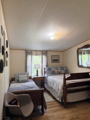 Ein Schlafzimmer mit zwei Betten, einem Schreibtisch, einem Stuhl, einem Spiegel und einem Fenster mit Vorhängen.