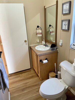 Ein Badezimmer mit einem Holzkosmetikschrank, einem weißen Waschbecken, einem Spiegel, einer Toilette und einem Handtuchhalter mit einem blumigen Handtuch.