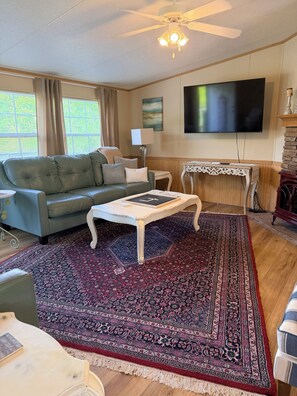 Ein Wohnzimmer mit einer Couch, Couchtisch, einem gemusterten Teppich, Fernseher und Deckenventilator.