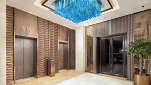 A modern hotel lobby with two elevators, a blue decorative ceiling feature, and a potted plant. - Shunhe Tianxi Hotel (Jinan Station, Jinan Maternal & Child Health Hospital) (Jinan)