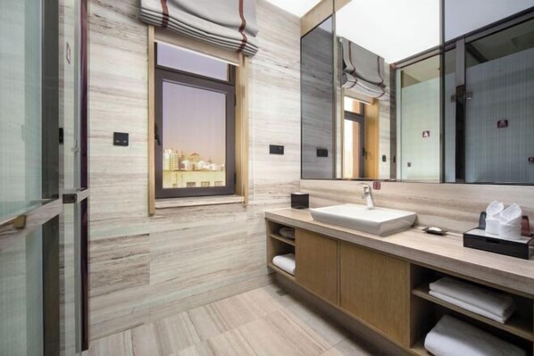 A modern bathroom with a large mirror, a sink, and a window with a view of buildings.