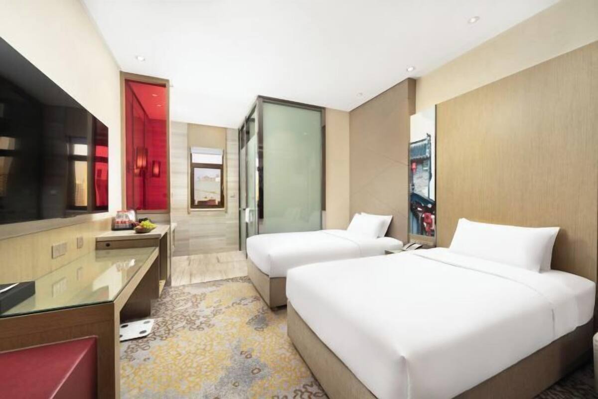 A hotel room with two beds, a desk, a TV, and a red door.