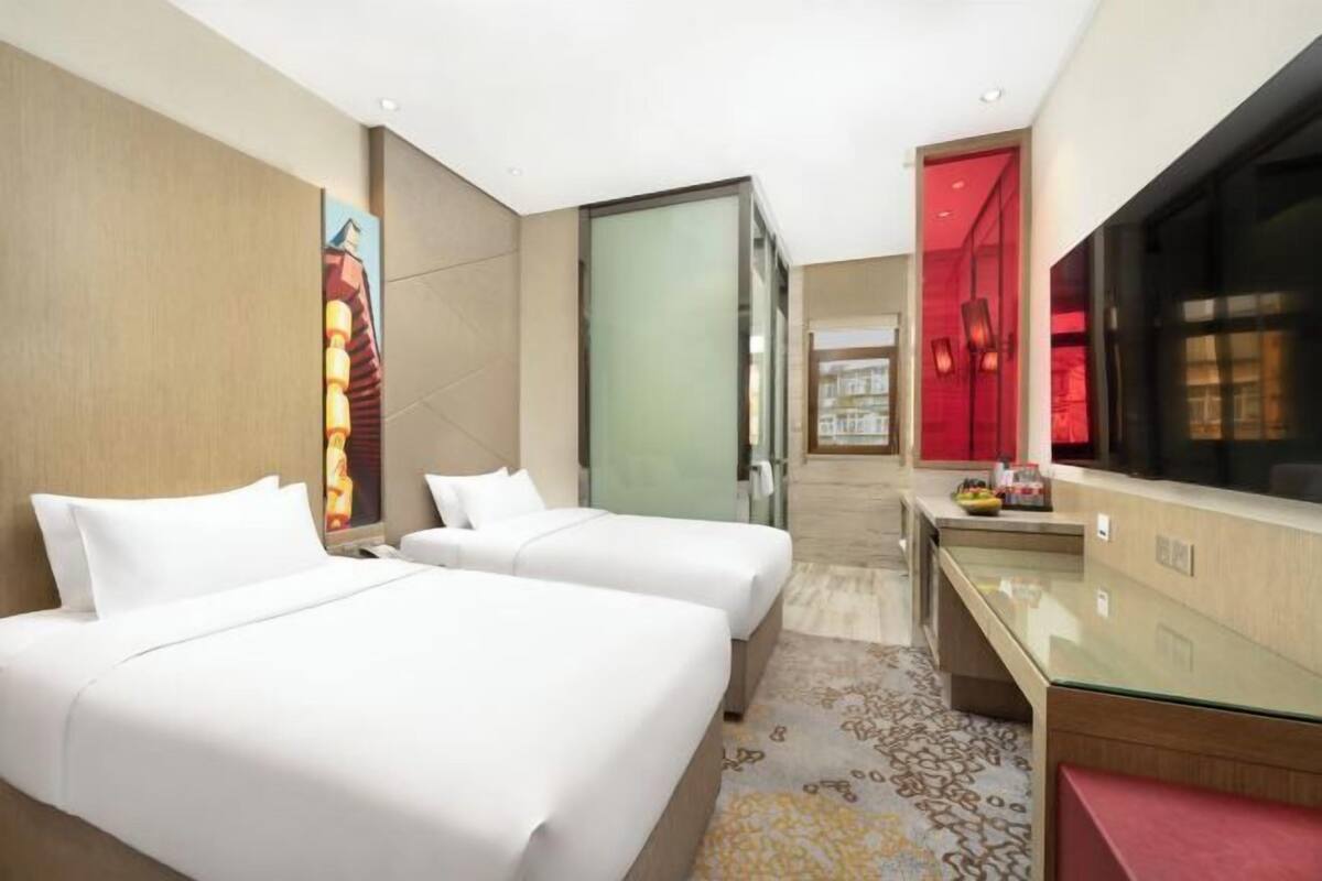 A hotel room with two beds, a desk, a TV, and a painting on the wall.