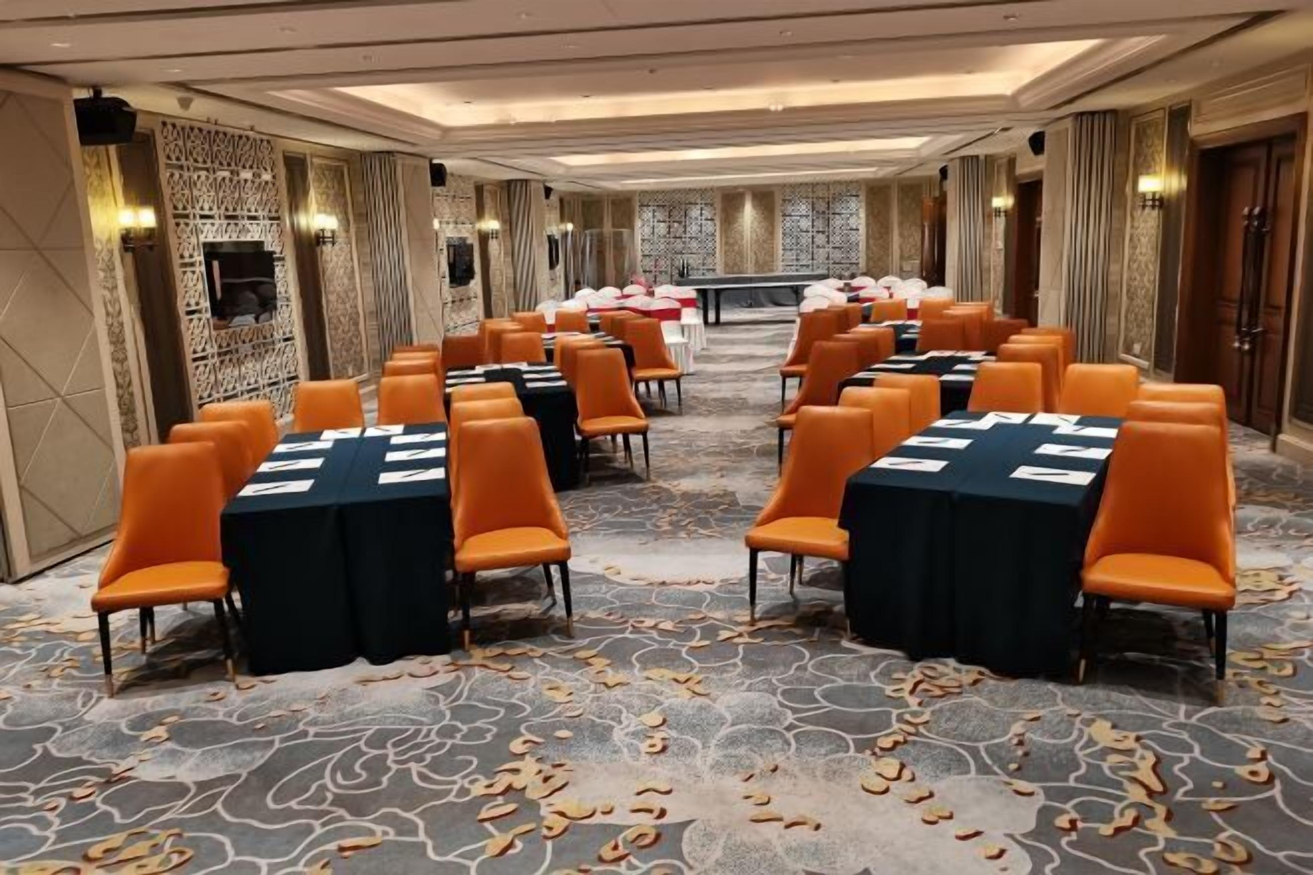A conference room with multiple tables and chairs, arranged in rows, with a patterned carpet and decorative wall panels.
