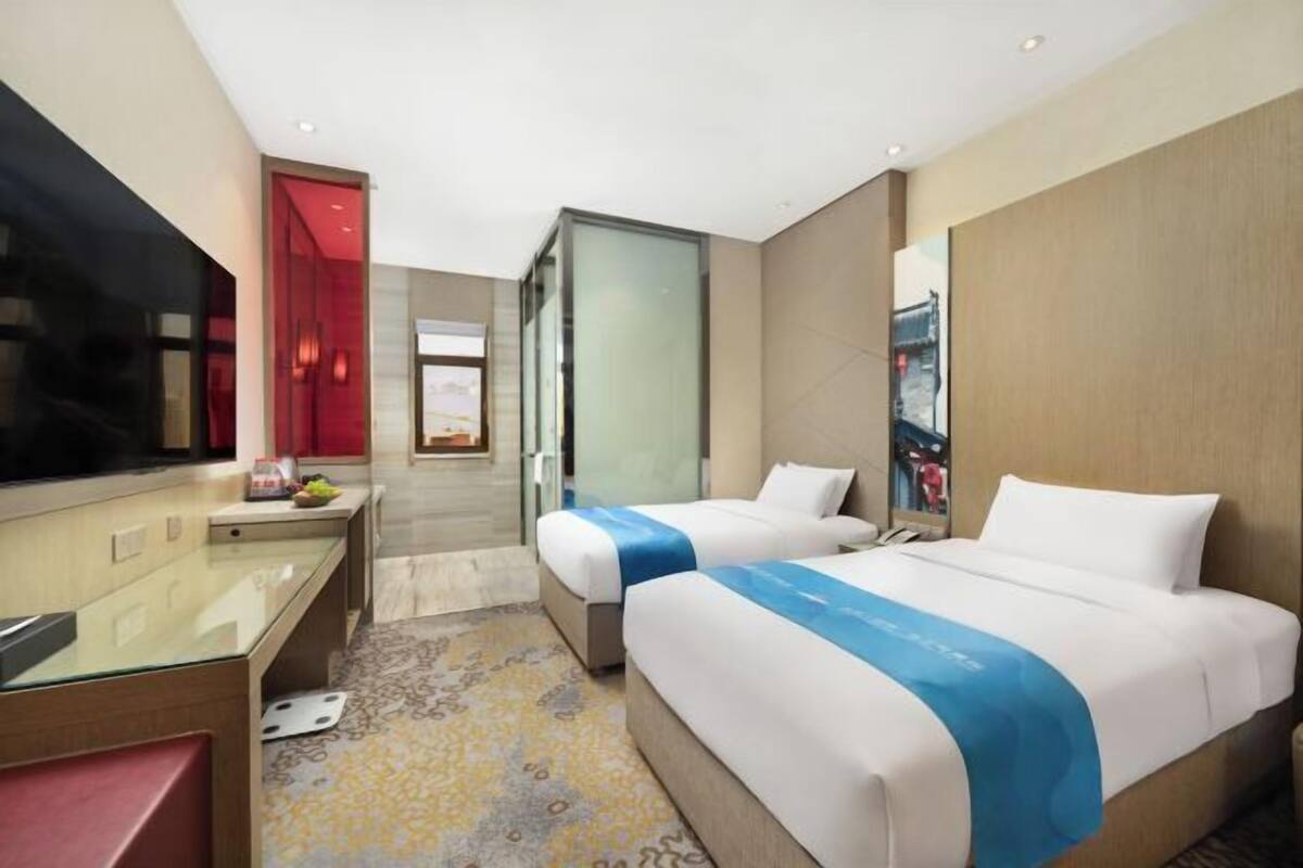 A hotel room with two beds, a TV, a desk, and a bathroom.