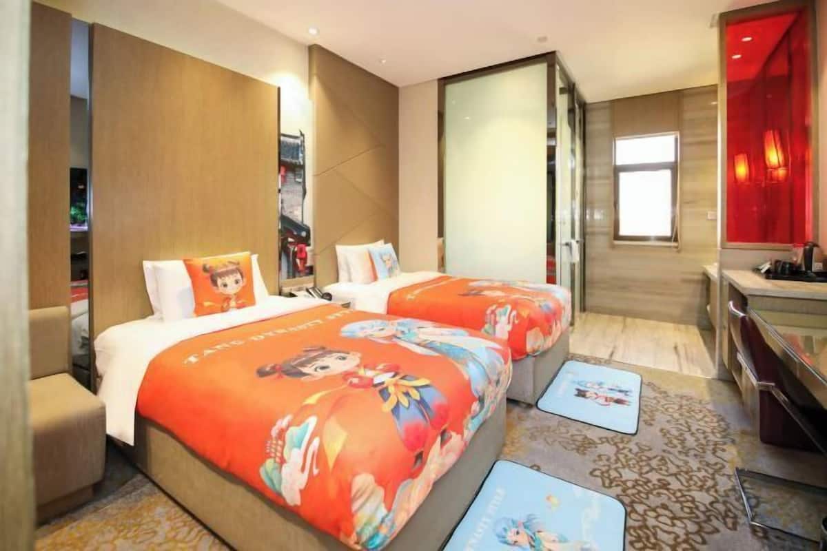 A hotel room with two beds, a desk, a chair, and a large window.