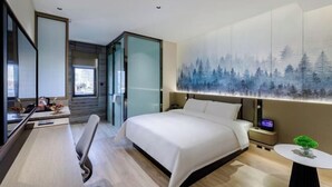A modern hotel room with a large bed, a desk with a chair, a small table with a plant, and a large wall painting of a forest. - Shunhe Tianxi Hotel (Jinan Station, Jinan Maternal & Child Health Hospital) (Jinan)