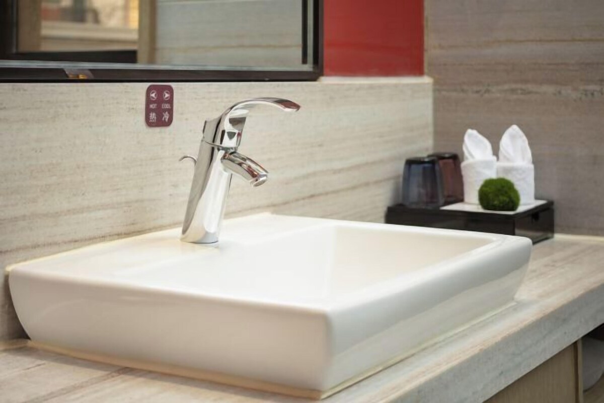 A modern bathroom with a rectangular white sink, chrome faucet, and a small potted plant on the counter.