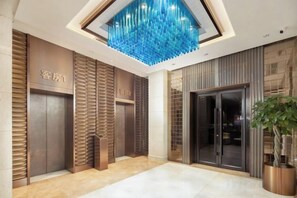 A hotel lobby with a modern design, featuring a large blue chandelier, a reception desk, and a potted plant. - Shunhe Tianxi Hotel (Jinan Station, Jinan Maternal & Child Health Hospital) (Jinan)