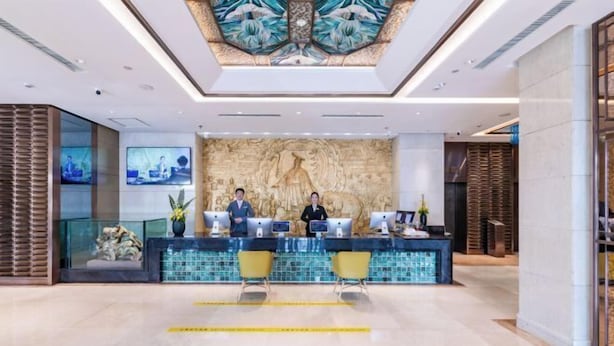 A reception area with a marble counter, two receptionists, and a decorative wall. - Shunhe Tianxi Hotel (Jinan Station, Jinan Maternal & Child Health Hospital) (Jinan)