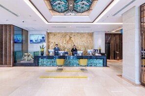 A reception area with a marble counter, two receptionists, and a decorative wall. - Shunhe Tianxi Hotel (Jinan Station, Jinan Maternal & Child Health Hospital) (Jinan)