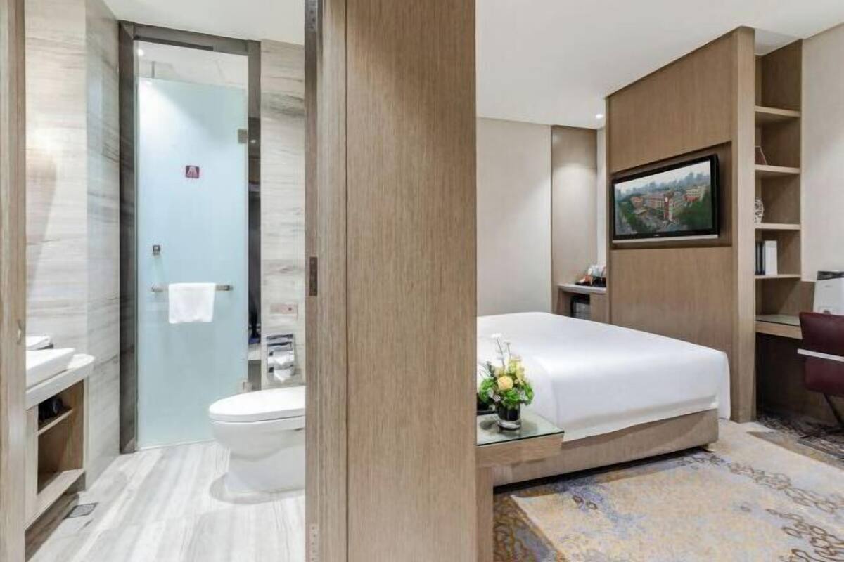 A hotel room with a bed, a television, a desk, a chair, and a bathroom with a toilet and sink.