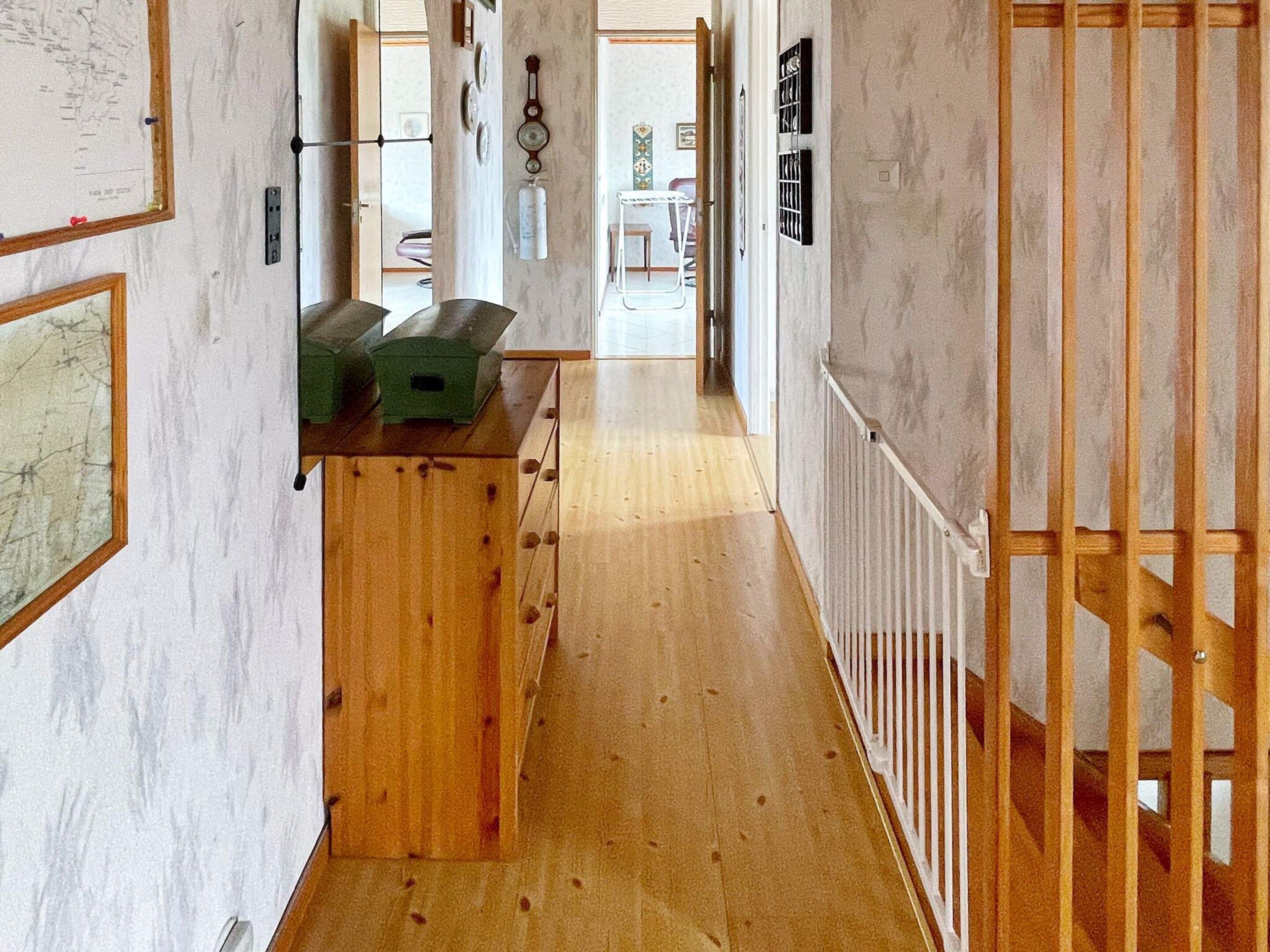 Een hal met houten vloer, een houten bankje en een radiator aan de rechterkant.