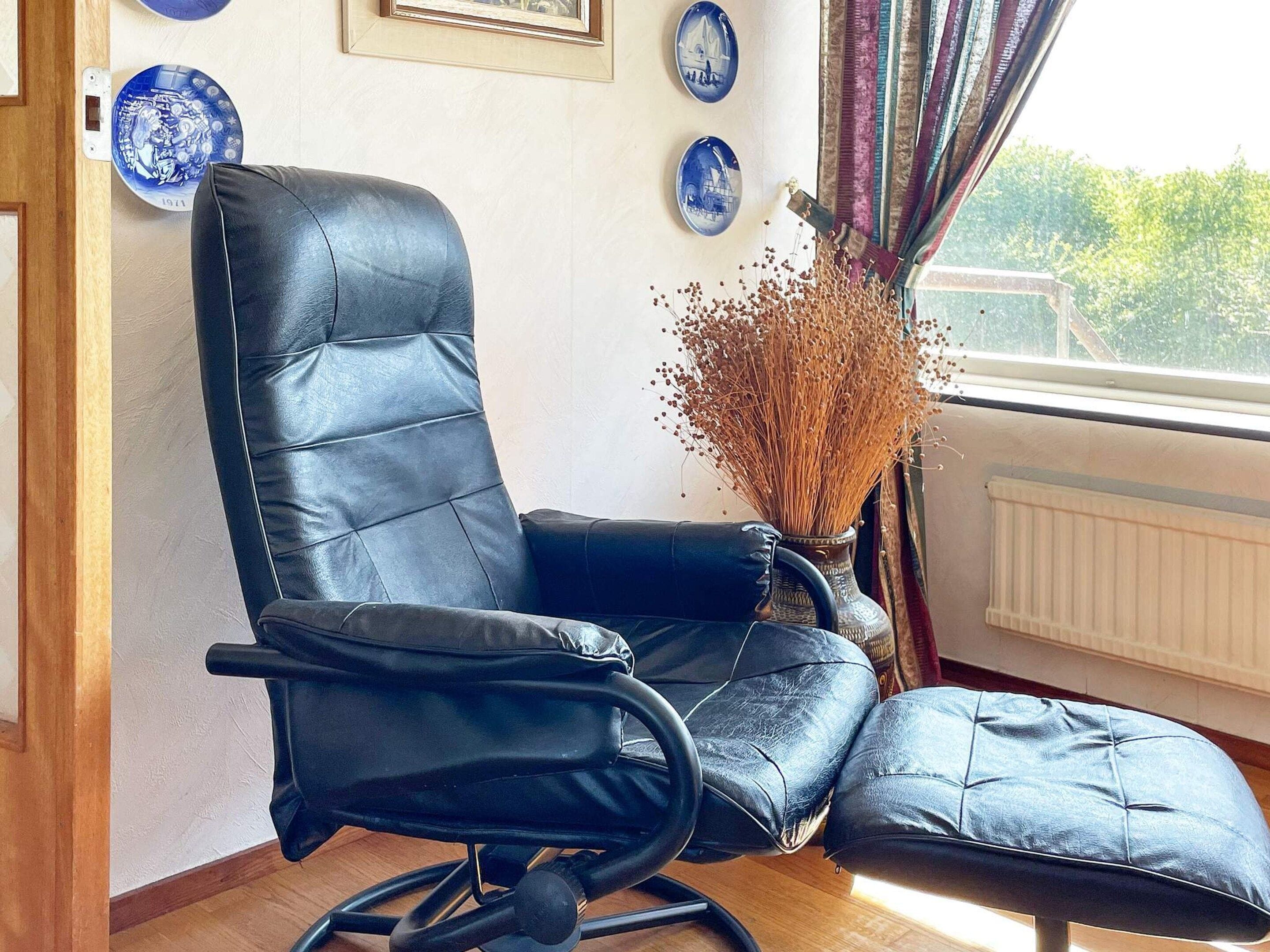 A black leather chair with a footrest, positioned near a window with a view of greenery.