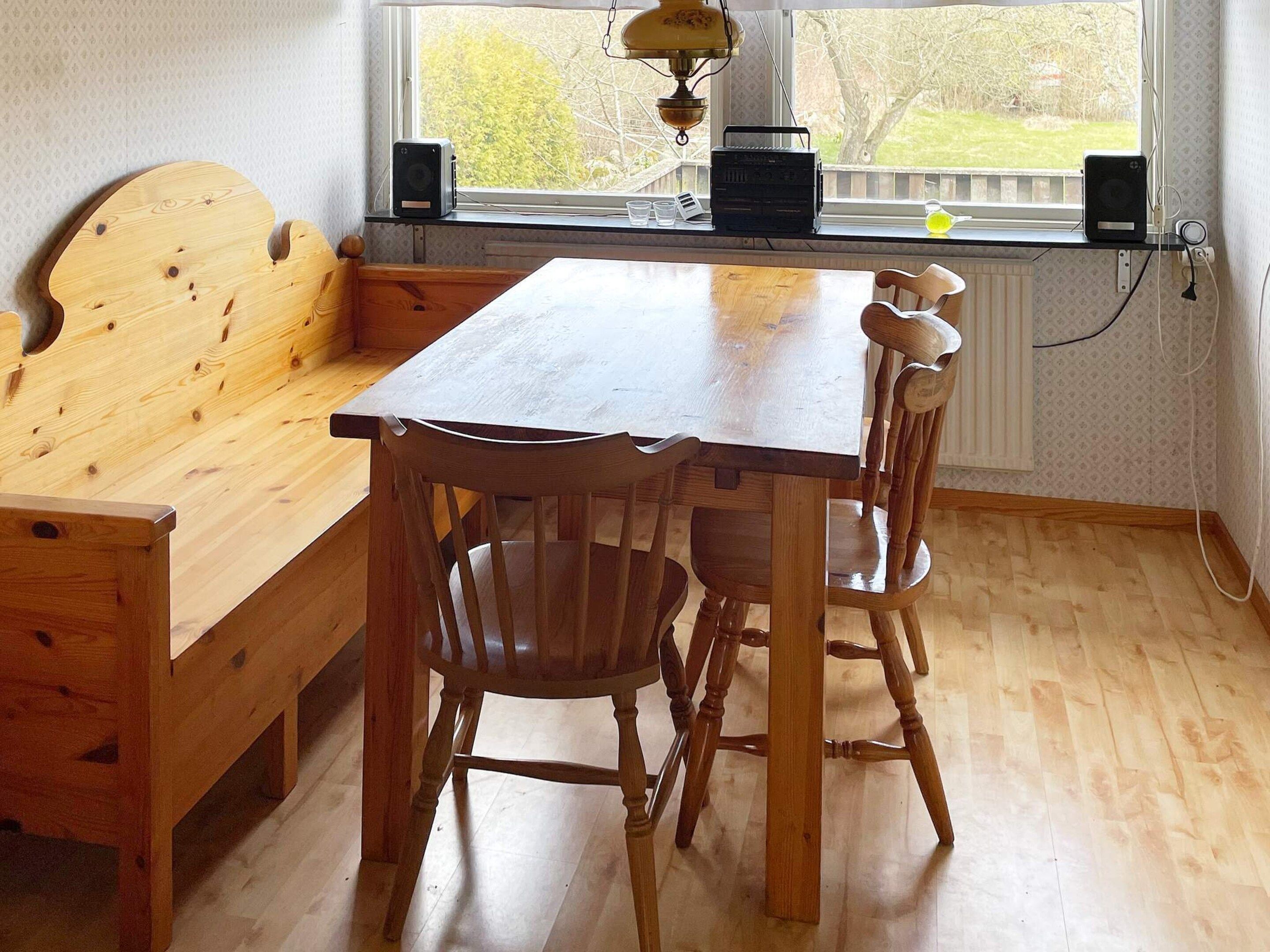 A wooden dining table with chairs, a bench, and a window with a view of trees.