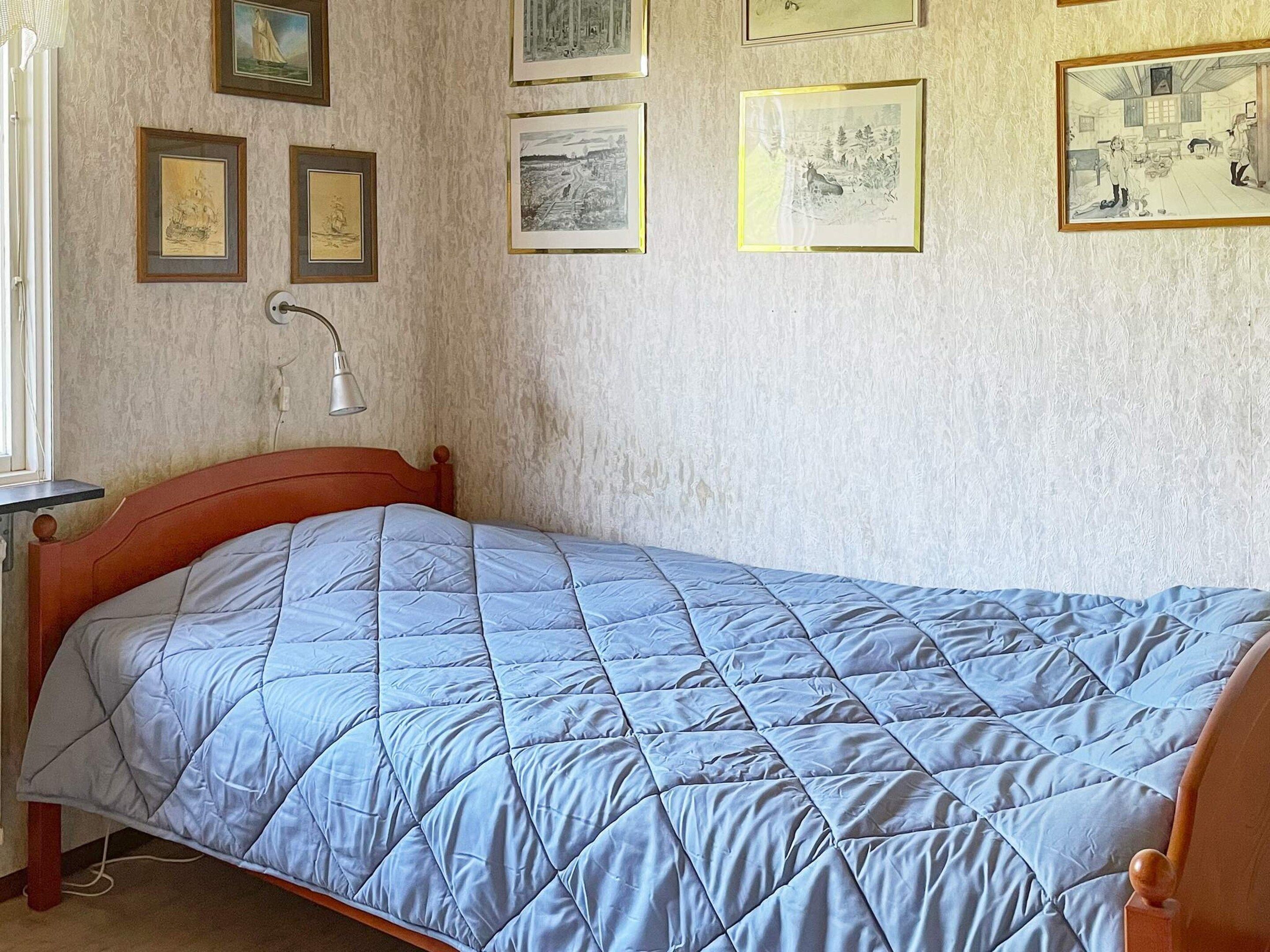 A bedroom with a single bed, a bedside table, and a lamp. There are framed pictures on the wall.