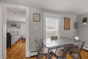 Un comedor con una mesa y sillas, una ventana con persianas y una planta en un estante.