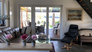 Una sala de estar moderna con un sofá, sillas, una mesa de centro de vidrio y plantas en macetas.
