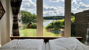 Un dormitorio con cama, ventana con vistas a un lago y jardín exterior.