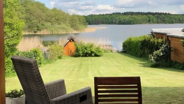 Un patio cubierto con sillas de mimbre y una mesa, con vistas a un lago y una zona verde.