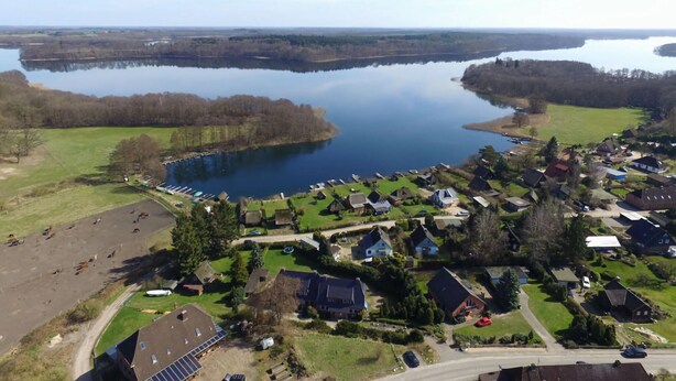 Vista aérea de un pueblo a orillas de un lago, con casas, un muelle y una carretera.