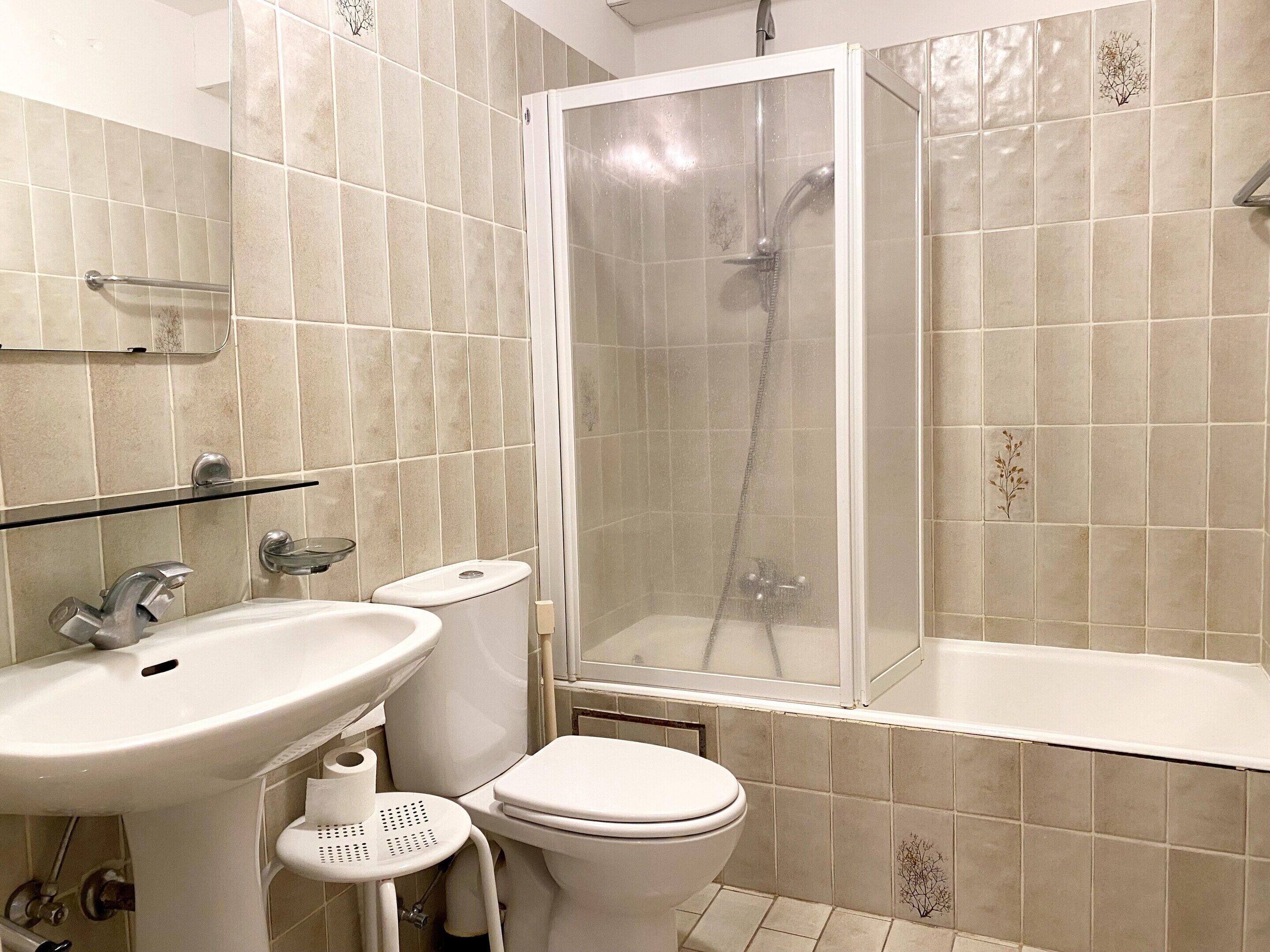 A bathroom with a shower, toilet, sink, and glass shelf.