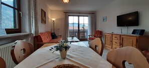 Un coin repas comprenant une table, des chaises, un vase de fleurs, un canapé, un téléviseur et une vue par la fenêtre.