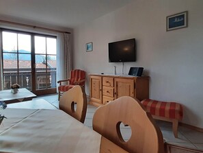 A room with a dining table, chairs, a bench, a TV, and a wooden cabinet. - Charmante Ferienwohnung in Bayrischzell (Bayrischzell)