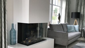 A modern living room with a white fireplace, a grey sofa, and a floor lamp. - Villa Bi de Kuhlung Comfortable Vacation Home (Rerik)