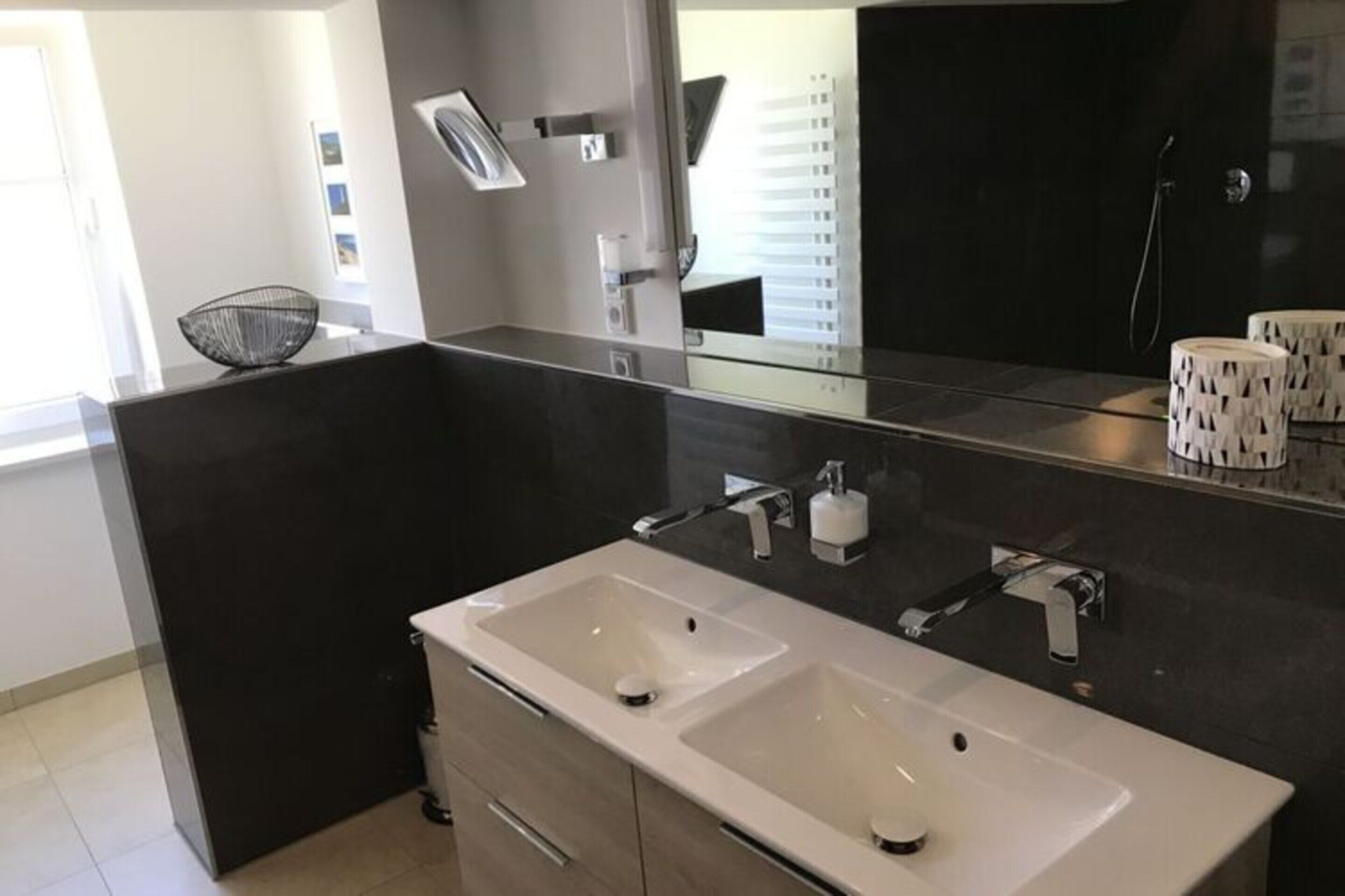 A modern bathroom with two sinks, a large mirror, and a dark tiled wall.