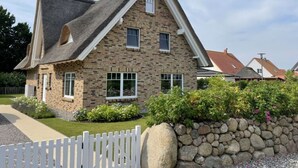 A stone house with a steeply pitched roof, a white picket fence, and a stone wall. - Villa Bi de Kuhlung Comfortable Vacation Home (Rerik)