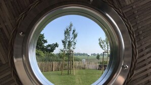 A circular window with a view of a grassy yard, a wooden swing set, and a fence. - Villa Bi de Kuhlung Comfortable Vacation Home (Rerik)