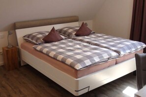 Un letto matrimoniale con una coperta a quadri e due cuscini marroni, un comodino con una lampada e un pavimento in legno.