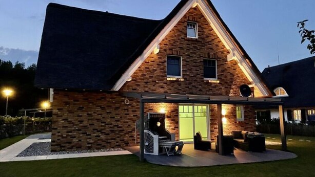 A modern house with a brick exterior, a covered patio with outdoor furniture, and a green door. - Villa Bi de Kuhlung Comfortable Vacation Home (Rerik)
